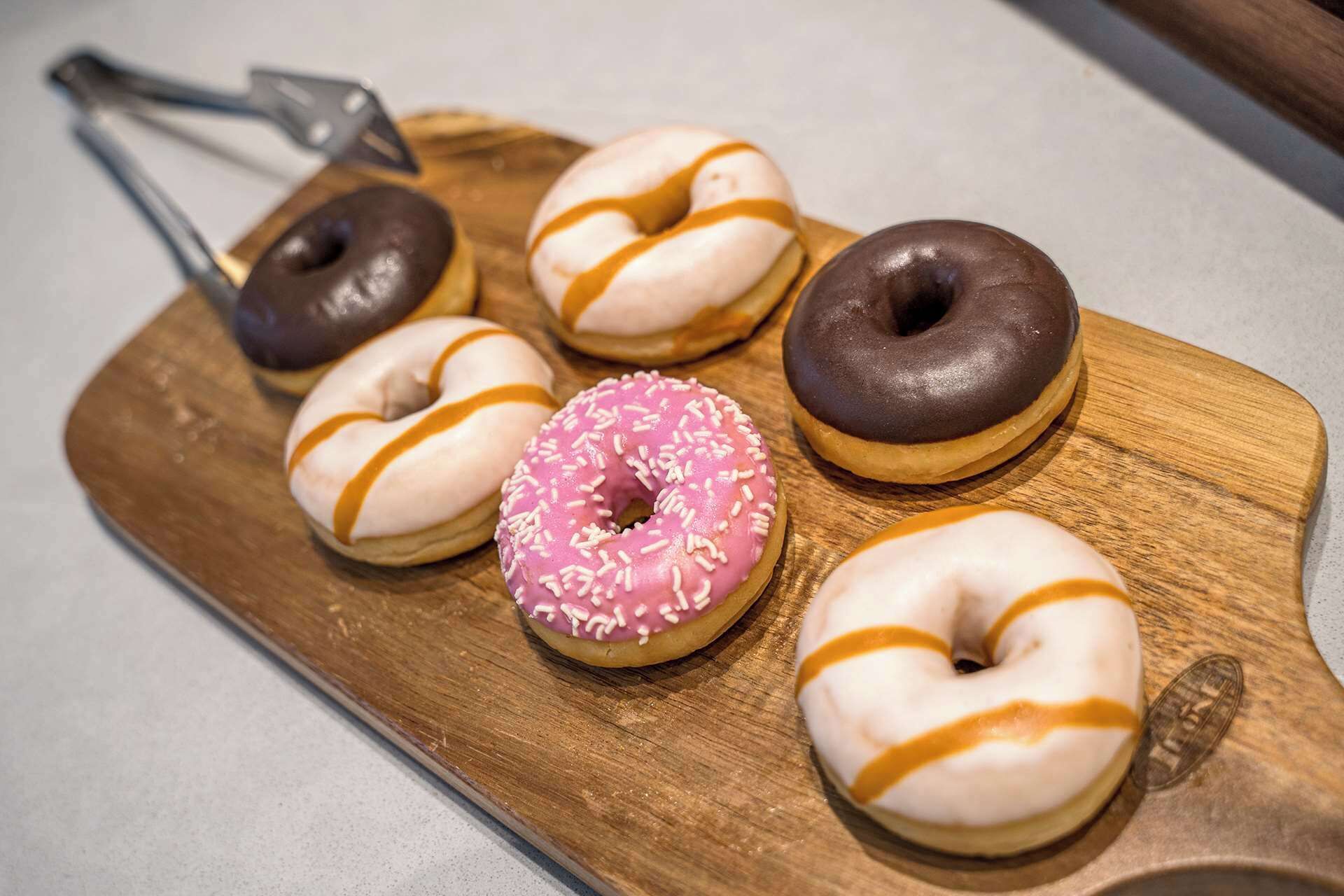 Six donuts on a wooden board.