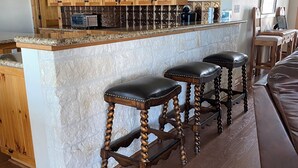 A kitchen with wooden cabinets, a stone island, and bar stools. - Turtle Bay Lodge 
Great for Large Gatherings (Port O'Connor)
