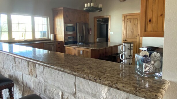 A kitchen with granite countertops, wooden cabinets, a large island, and a mounted deer head. - Turtle Bay Lodge 
Great for Large Gatherings (Port O'Connor)