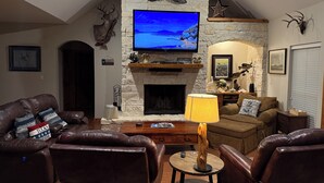 A cozy living room with leather sofas, a stone fireplace, a mounted TV, and deer antlers on the wall. - Turtle Bay Lodge 
Great for Large Gatherings (Port O'Connor)