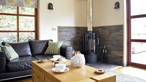 A modern living room with a leather sofa, a wooden coffee table with tea set, a fireplace, and a large window.