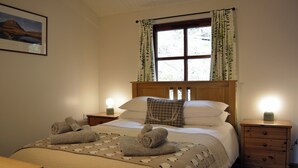 A neatly made bed with towels, a bedside table with a lamp, and a window with curtains.