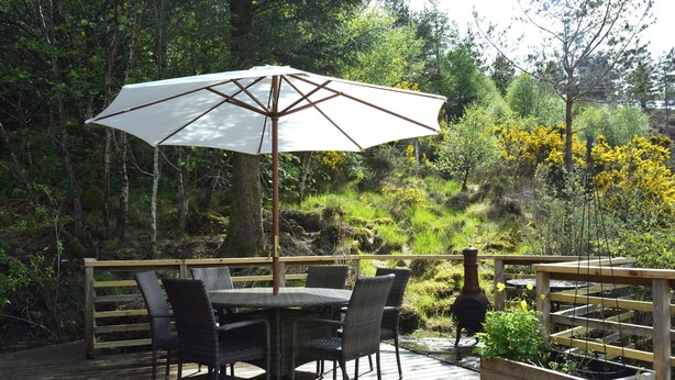 An outdoor deck with a table and chairs, an umbrella, and a planter with plants.