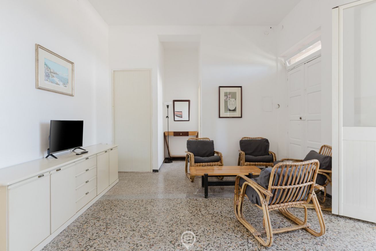 Una stanza con una televisione su un mobile bianco, un tavolo di legno con sedie e quadri appesi alle pareti.
