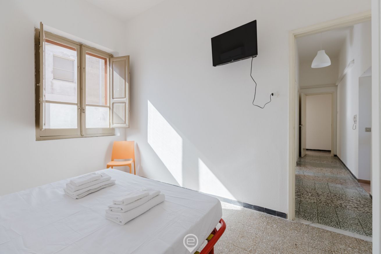 Une chambre d’hôtel avec un lit, un téléviseur fixé au mur, une fenêtre avec des stores et une chaise.