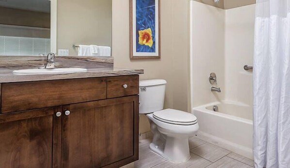 A bathroom with a wooden vanity, white toilet, and bathtub.