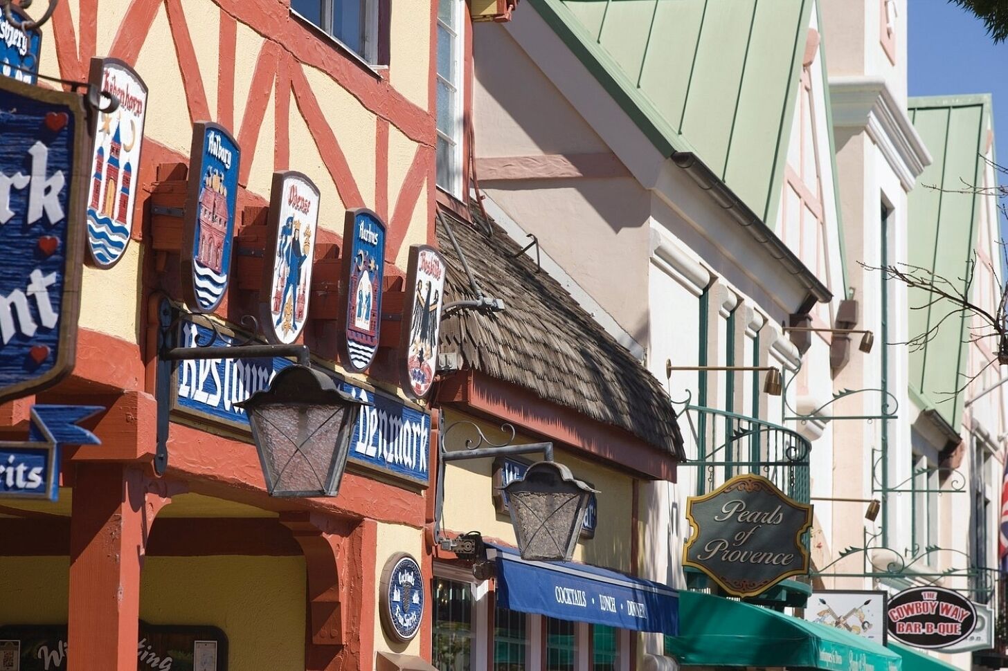 Una calle con varios comercios, incluyendo un bar llamado 'The Cowboy Way Bar-B-Que'.