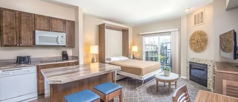 Habitación de hotel compacta con kitchenette, cama con vistas, comedor y chimenea.