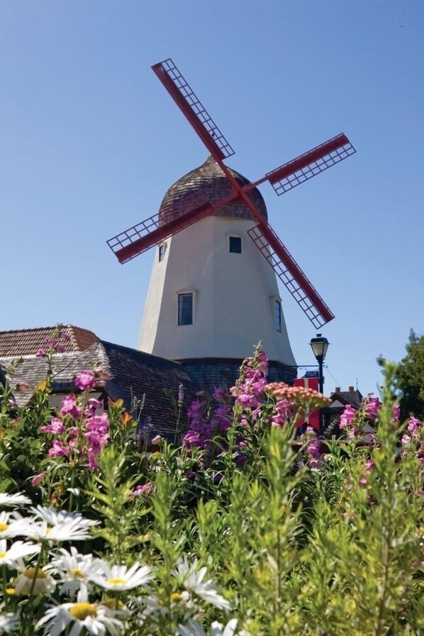 A windmill with a white body and red sails, surrounded by flowers and a clear blue sky.
