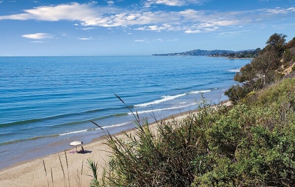 A beach with clear blue water, sandy shore, and greenery.