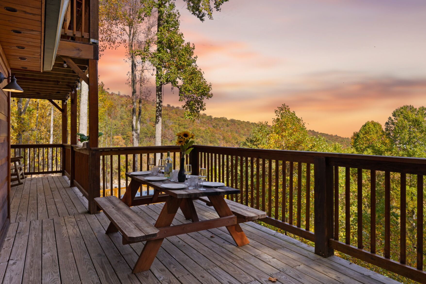 Una terraza de madera con mesas de picnic y barandilla, con vistas a un paisaje boscoso.