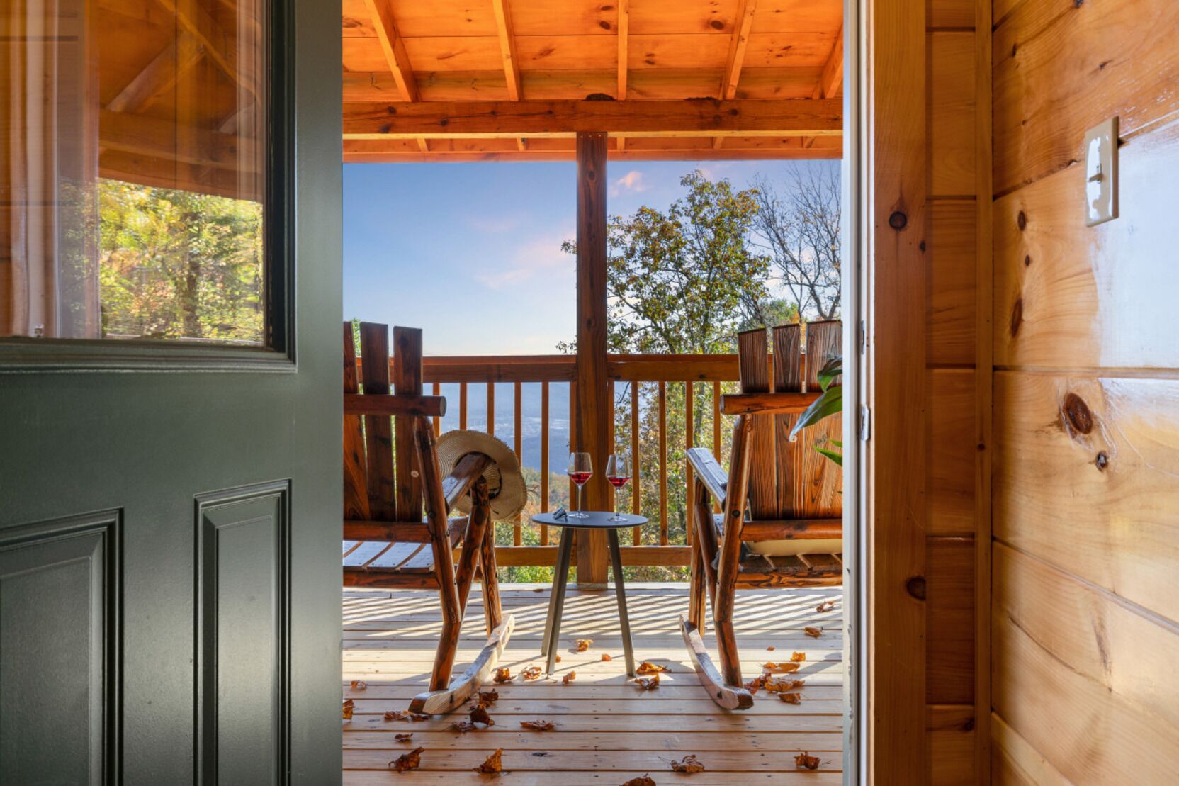 A wooden deck with a view of trees, a chair, and a table with a glass of wine.