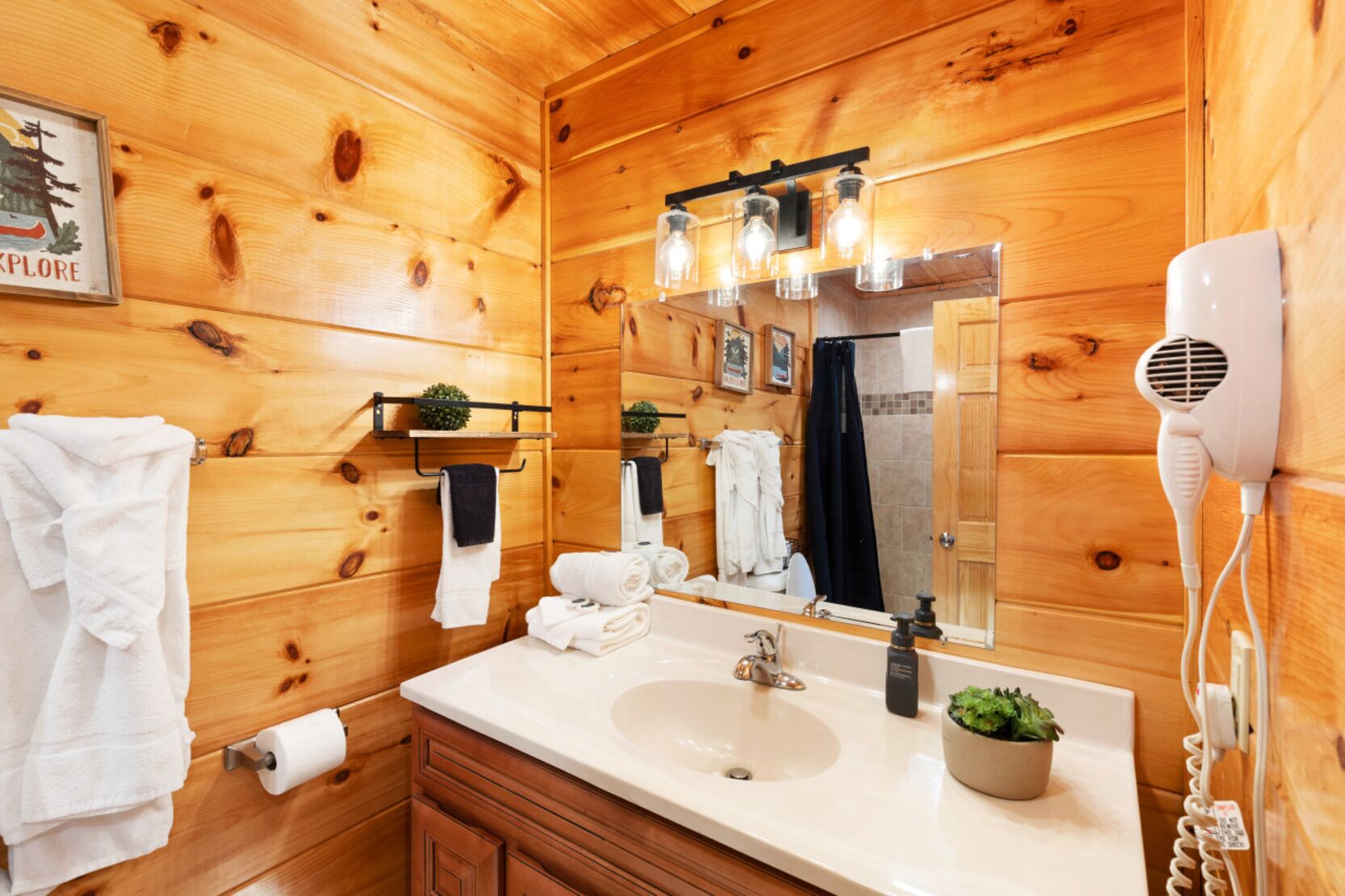 Ein Badezimmer einer Holzhütte mit Waschbecken, Spiegel, Handtuchhalter und einem Fön.