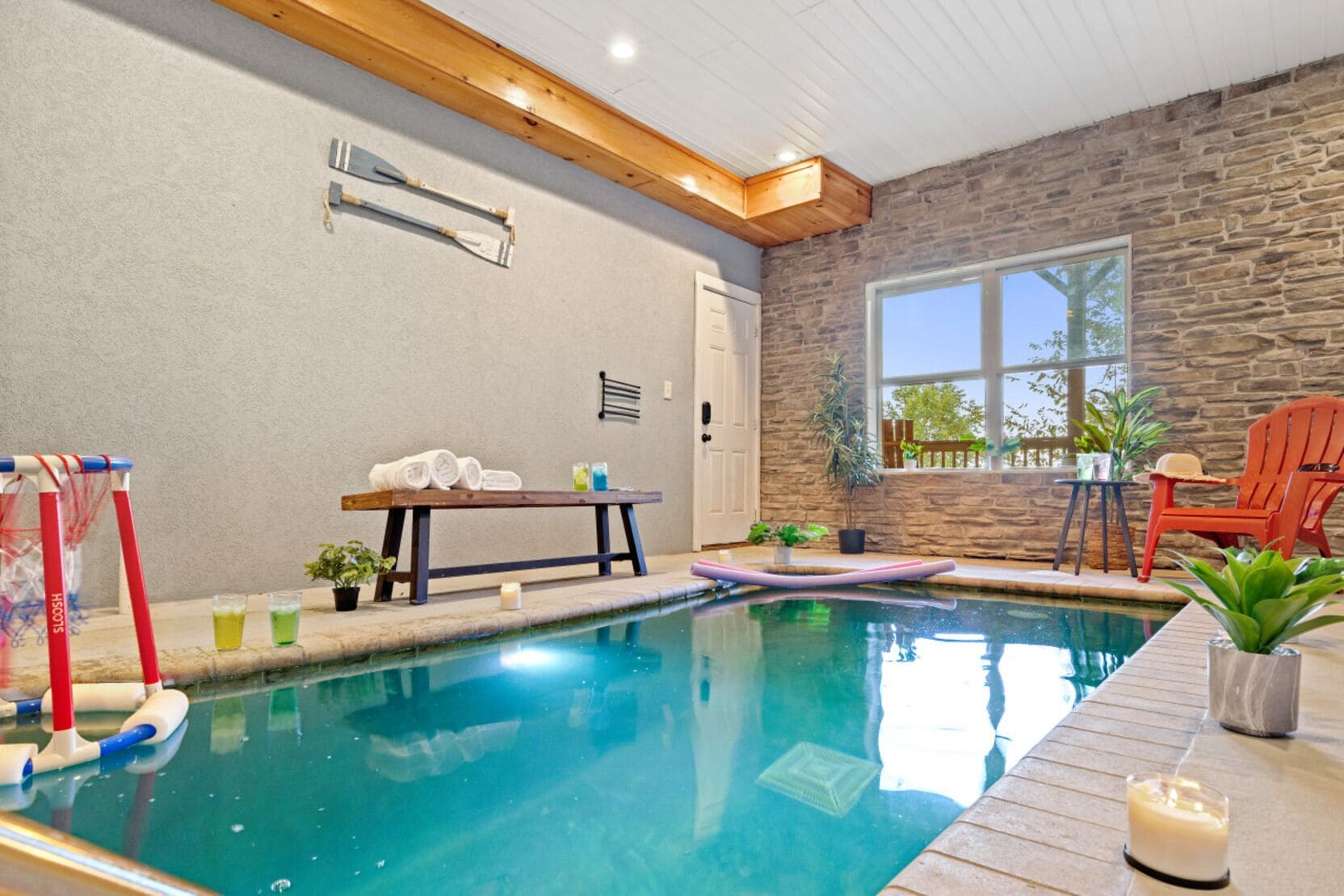Area piscina interna con parete in pietra, soffitto in legno e finestra.