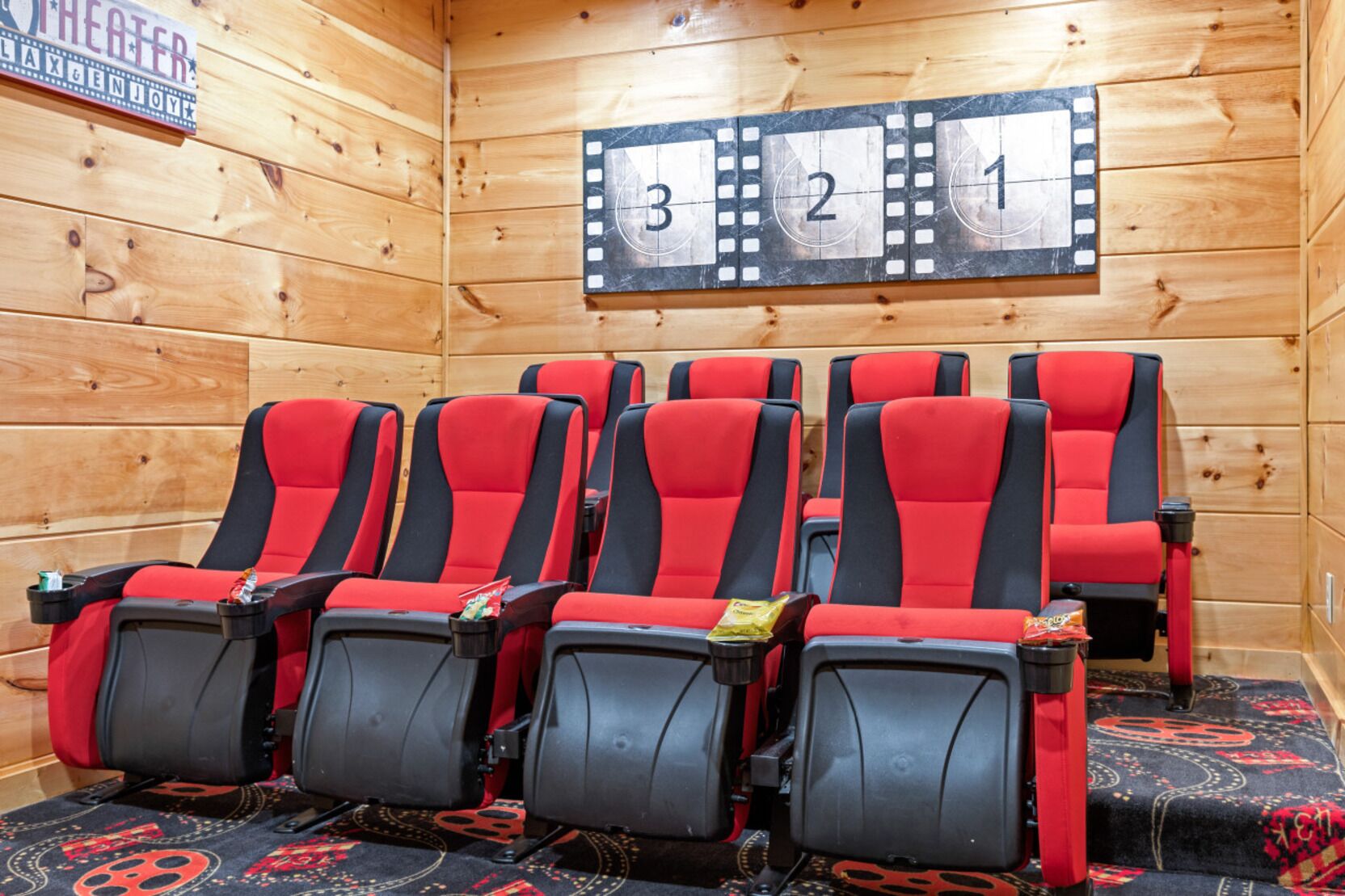 Una habitación con paneles de madera y seis asientos estilo teatro en rojo y negro, dispuestos en dos filas. En la pared se proyecta una franja de celuloide con los números 3, 2, 1.