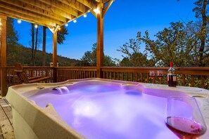 A hot tub with a wooden deck and string lights, surrounded by trees. - Serene Mountain Retreat by Ghosal Luxury Lodging (Sevierville)
