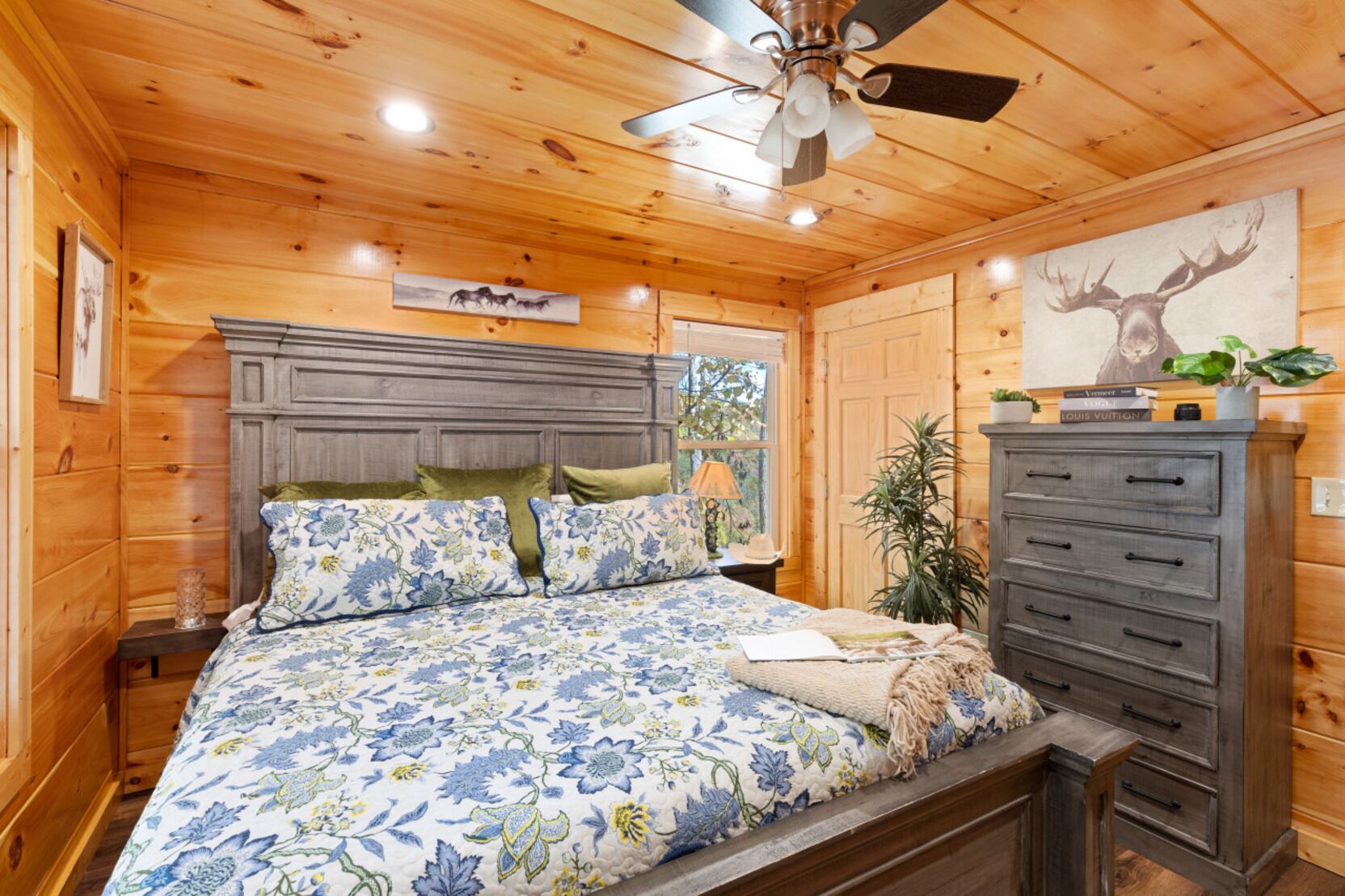 A wooden cabin bedroom with a bed, dresser, and ceiling fan.