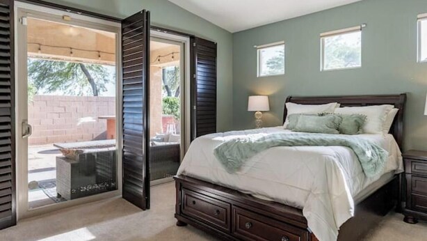 A bedroom with a large bed, a nightstand, a lamp, and a sliding glass door leading to an outdoor patio. - Elegant desert getaway. 4 bedroom 2.5 bath. Sleeps 8. Heated pool. Outdoor BBQ. (Oro Valley)