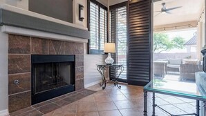 A living room with a fireplace, a glass coffee table, and a view of the outdoor patio. - Elegant desert getaway. 4 bedroom 2.5 bath. Sleeps 8. Heated pool. Outdoor BBQ. (Oro Valley)