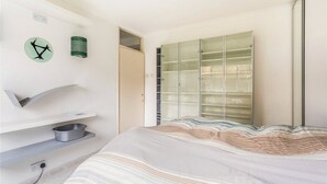 A bedroom with a bed, a small shelf with a basket, a clock, and a wardrobe with glass doors. - Central one bedroom flat. CONTACT ME BEFORE BOOKING TO CHECK AVAILABILITY (London)