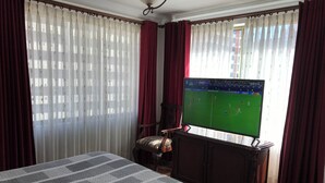 A hotel room with a bed, a television displaying a sports game, a chair, and curtains. - Private Apartment on Arce Avenue (La Paz)