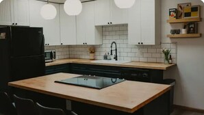 Eine moderne Küche mit weißen Schränken, einem schwarzen Kühlschrank, einer Mikrowelle, einem Waschbecken mit schwarzem Wasserhahn und einer Holzinsel mit Stühlen.