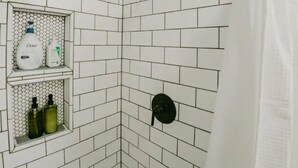 Ein Duschbereich mit weißen Fliesen, einem schwarzen Duschkopf und einem Ablagefach für Toilettenartikel.