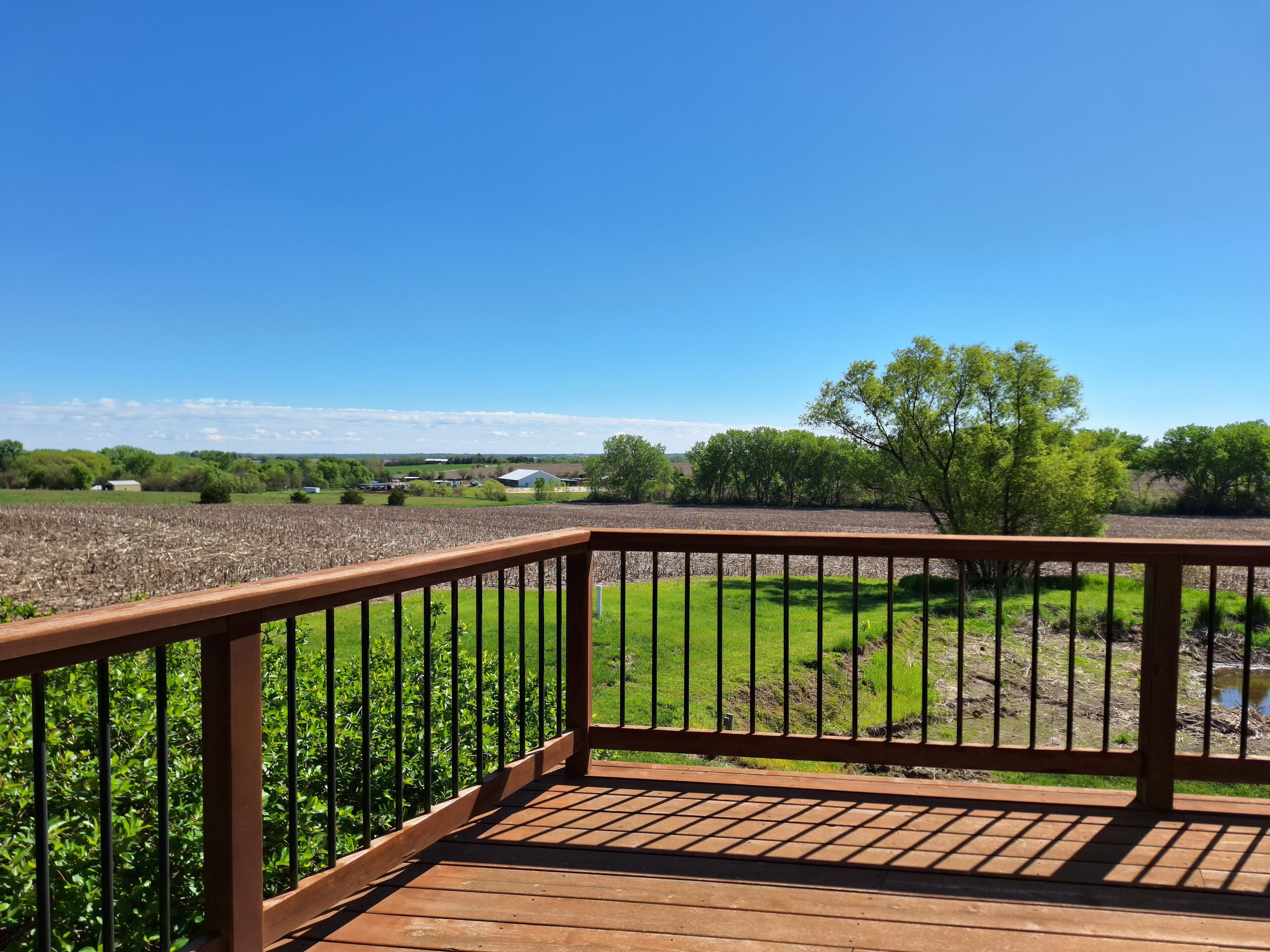 A wooden deck with a metal railing overlooking a grassy field and a distant building.
