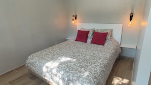 A bedroom with a bed, two red pillows, a patterned bedspread, and two wall-mounted light fixtures.
