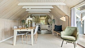 A spacious attic bedroom with a wooden ceiling, a dining area with a wooden table and chairs, a green armchair, and a view of the kitchen through a large window. - 2 bedroom beautiful home in Farsø (Farsø)