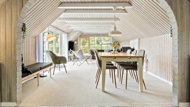 A spacious dining area with a high ceiling and wooden beams, featuring a central table with chairs and a bench along the wall. - 2 bedroom beautiful home in Farsø (Farsø)