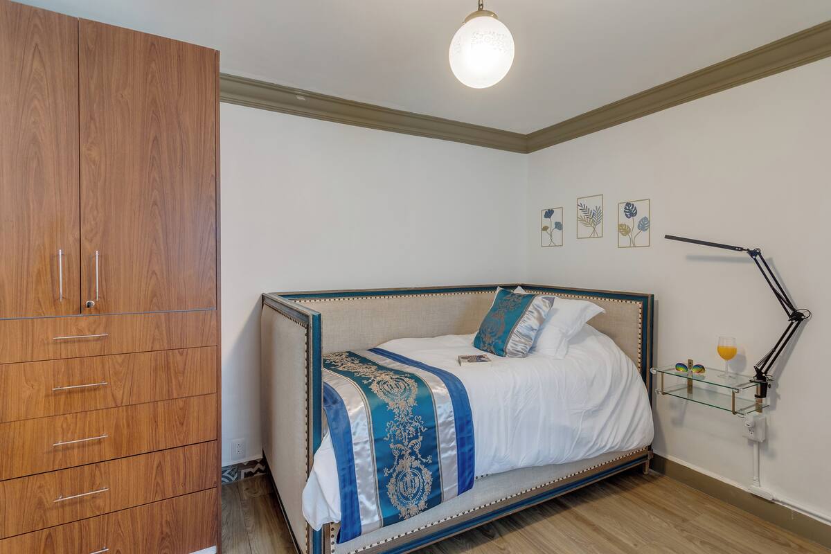 A bedroom with a bed, a wardrobe, a bedside table with a lamp, and wall art.