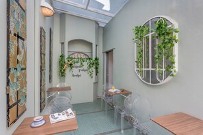 A cozy cafe with clear glass tables, a wooden bench, and a wall adorned with greenery and a 'grateful' sign. - CONDESA HOUSE (Mexico City)