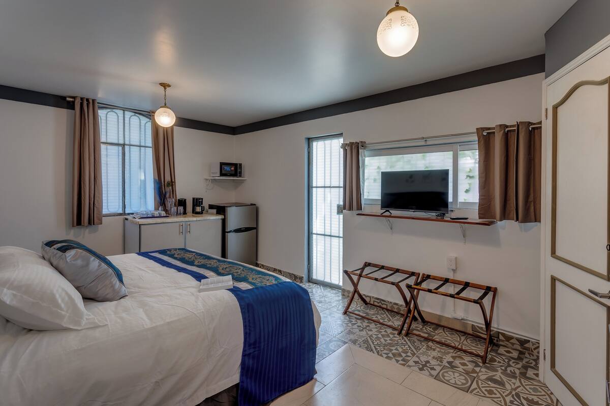 A bedroom with a bed, bedside table, TV, and a small kitchenette.