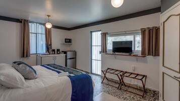 A bedroom with a bed, bedside table, TV, and a small kitchenette.