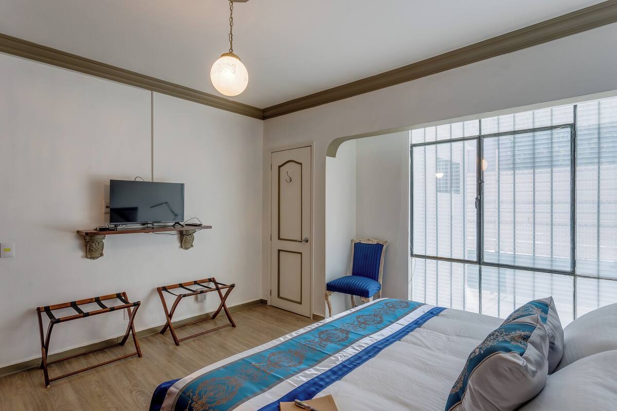 A bedroom with a bed, a TV on a shelf, a chair, and a window with a view.