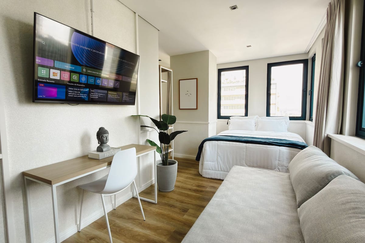Ein Hotelzimmer mit Bett, Schreibtisch, Stuhl, einem an der Wand montierten Fernseher und einem Fenster.