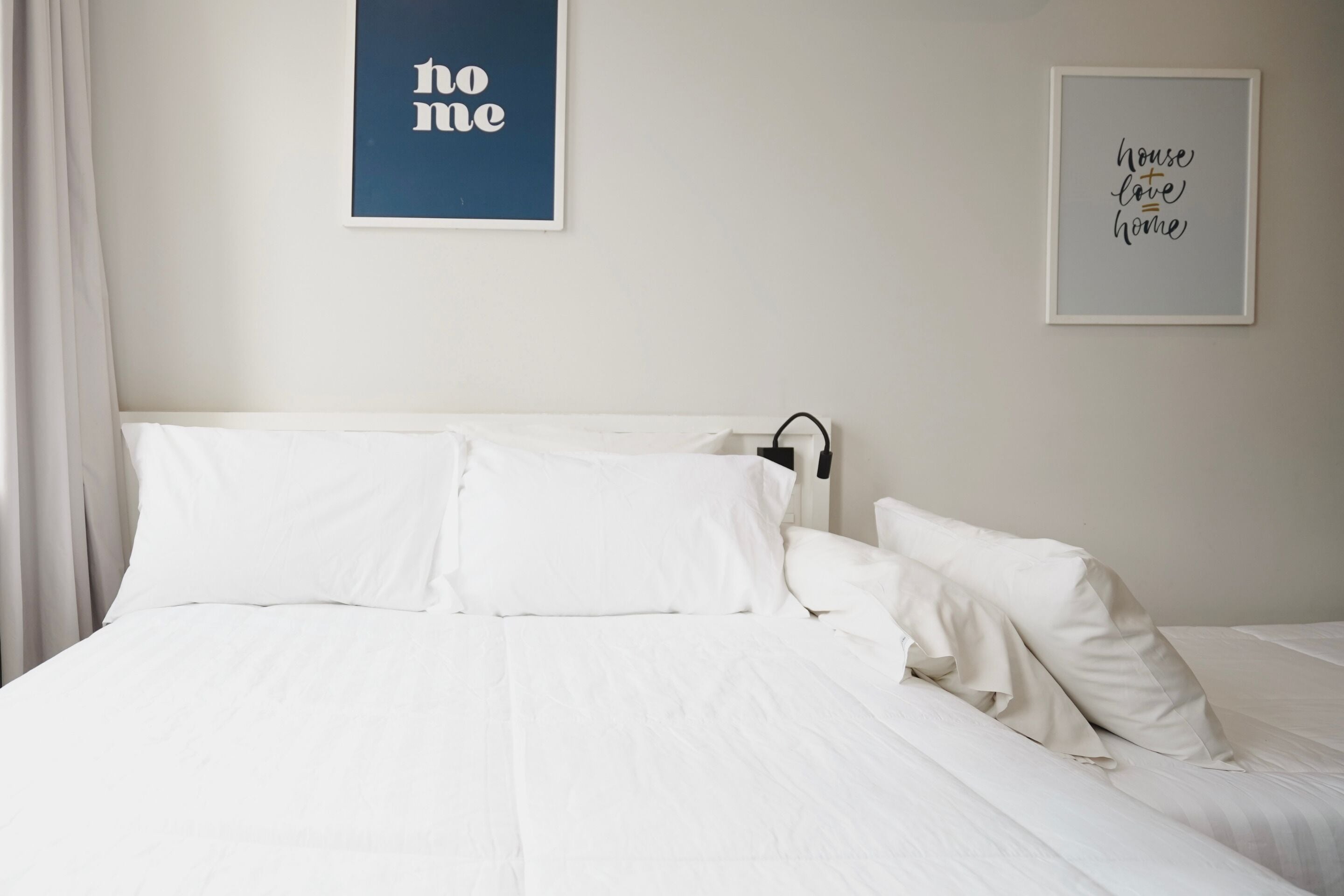 A neatly made bed with white linens and pillows, a framed quote on the wall, and a simple, clean room design.