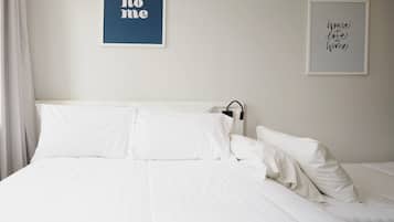 A neatly made bed with white linens and pillows, a framed quote on the wall, and a simple, clean room design.