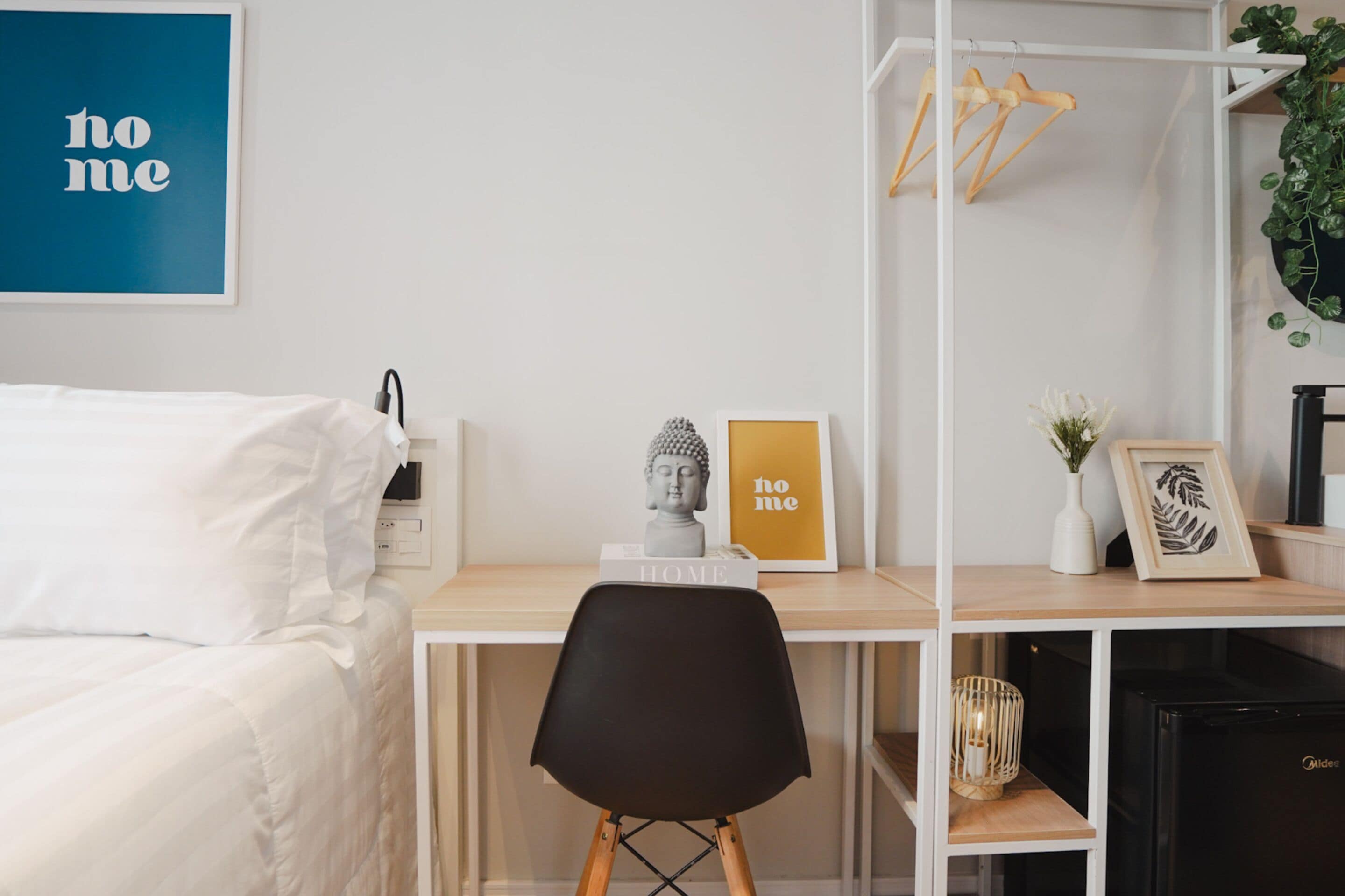 Ein Schlafzimmer mit einem Bett, einem Schreibtisch mit Stuhl, einer kleinen Ablagefläche mit Dekoration und einer an der Wand befestigten Pflanze.