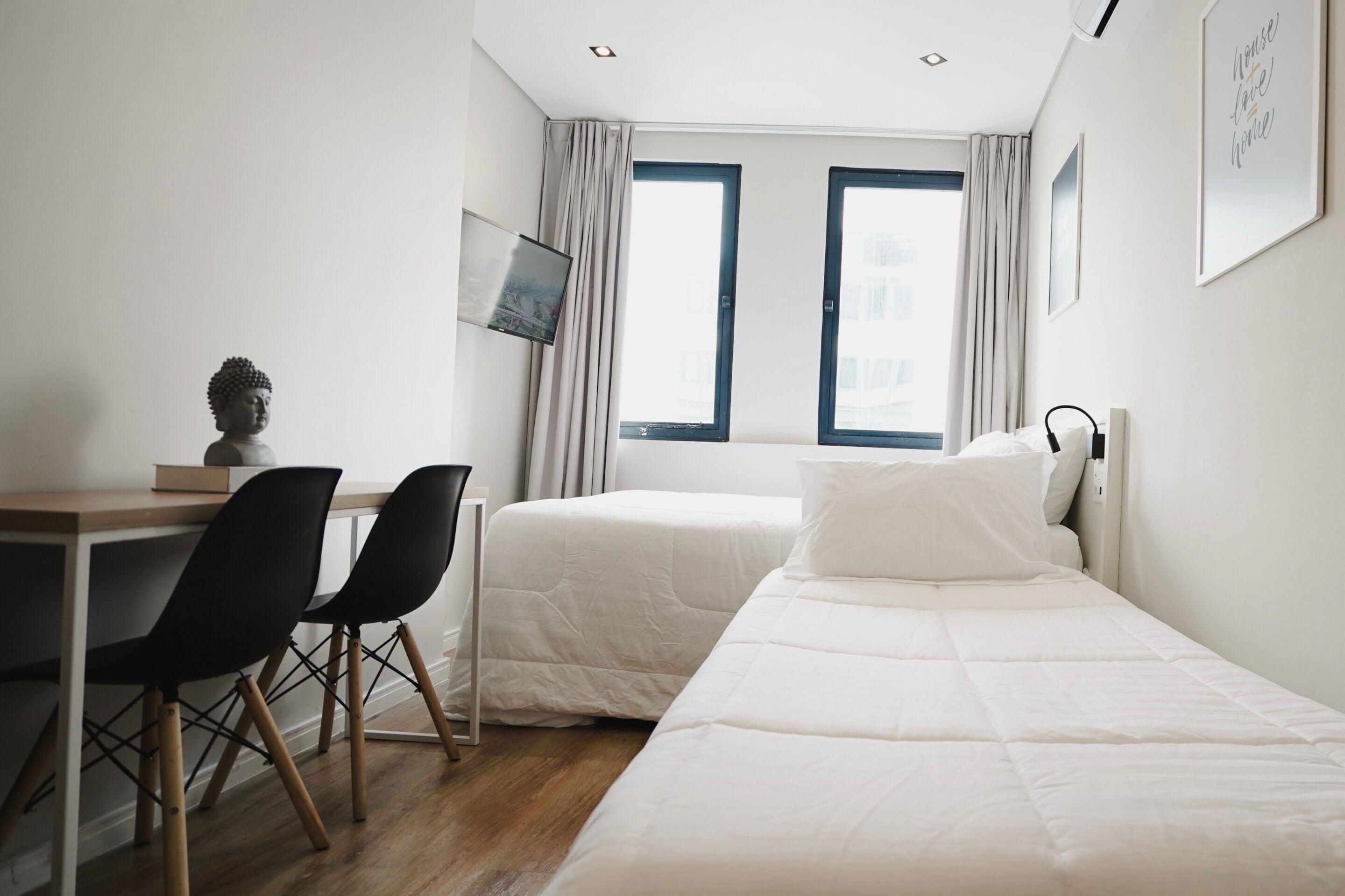 A hotel room with a desk, two beds, a chair, and a window with curtains.