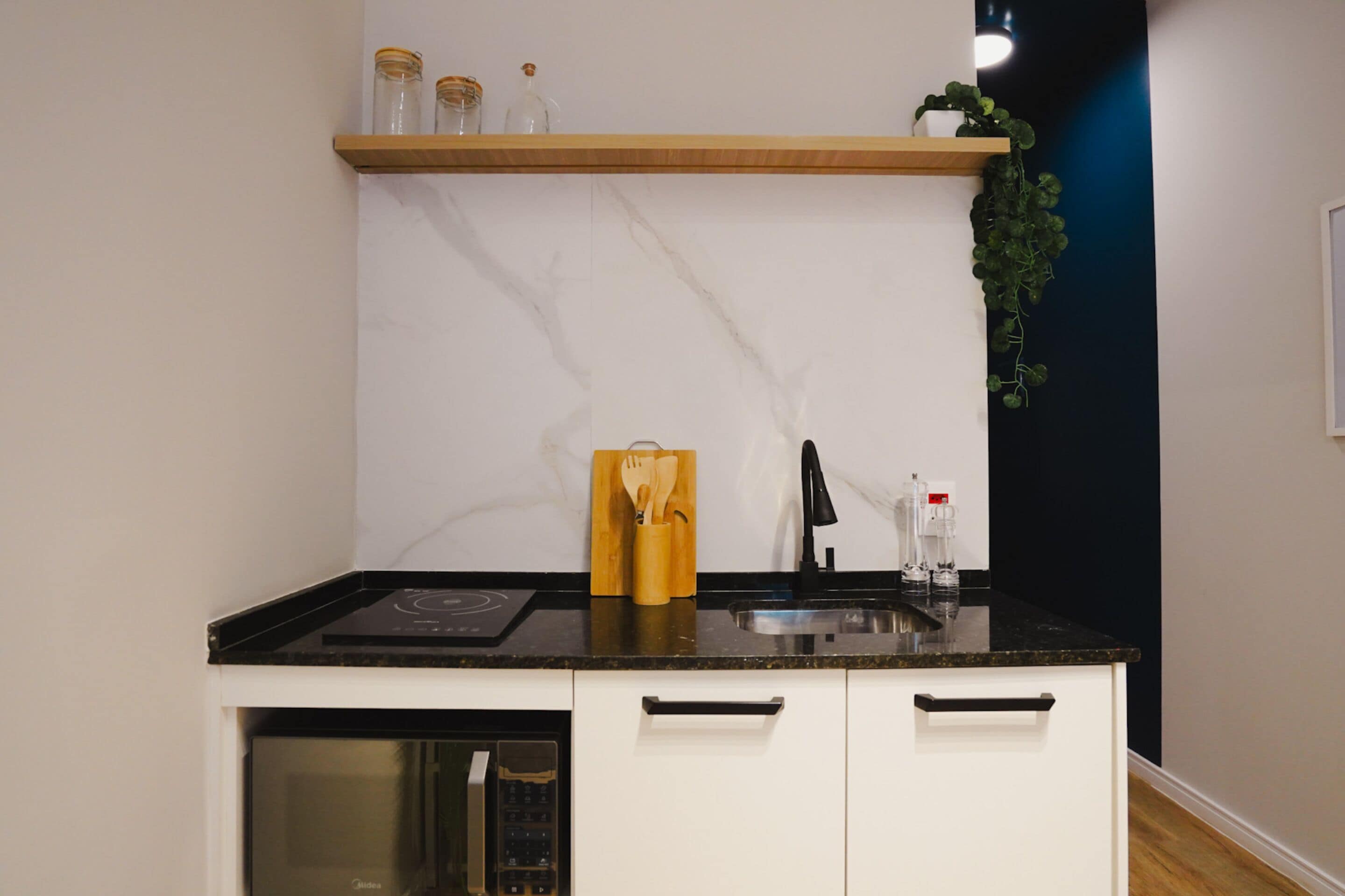 A kitchen with a black countertop, white cabinets, a built-in oven, and a wooden shelf above the sink.