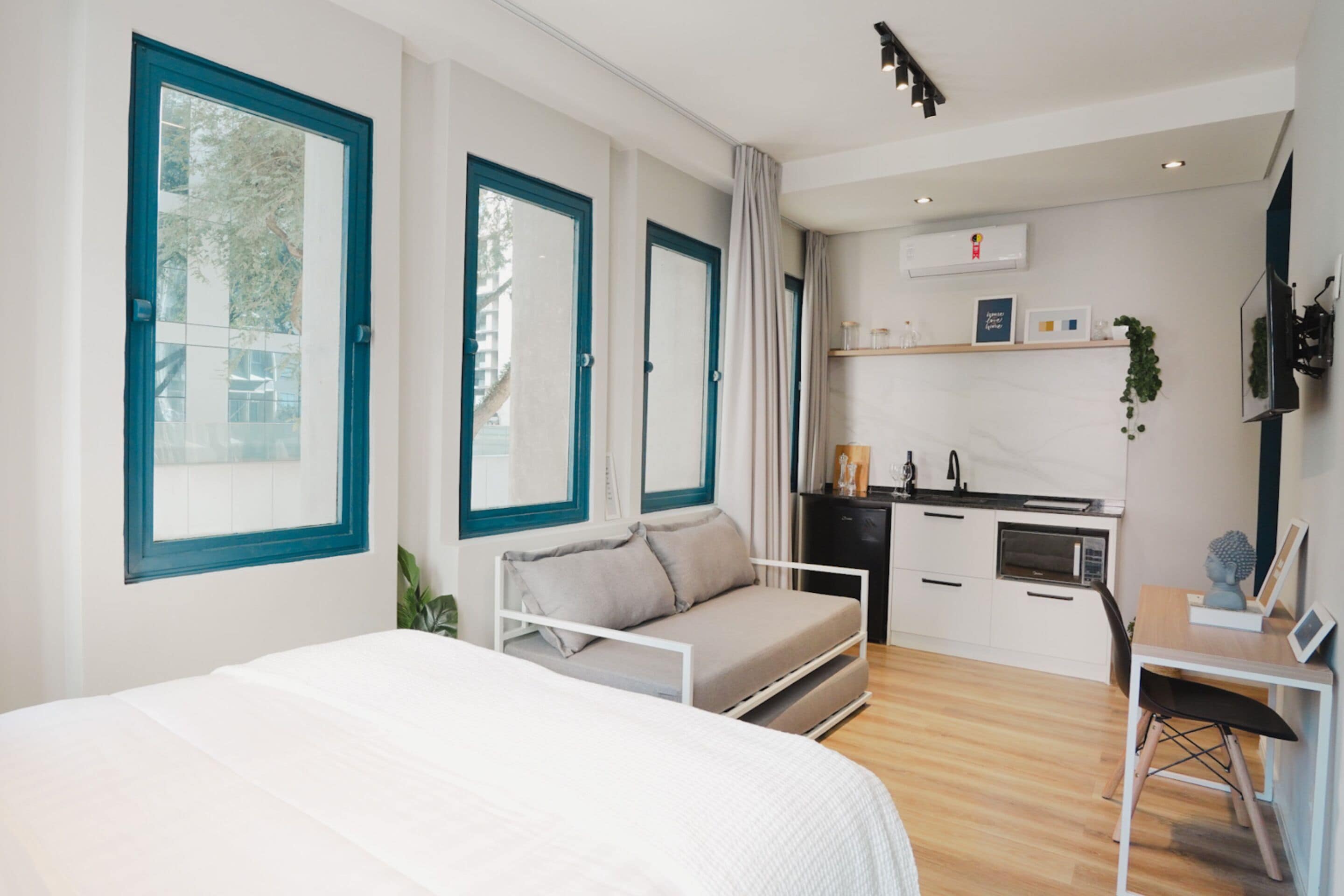 A modern hotel room with a bed, a sofa, a desk, and a kitchenette.