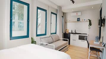 A modern hotel room with a bed, a sofa, a desk, and a kitchenette.