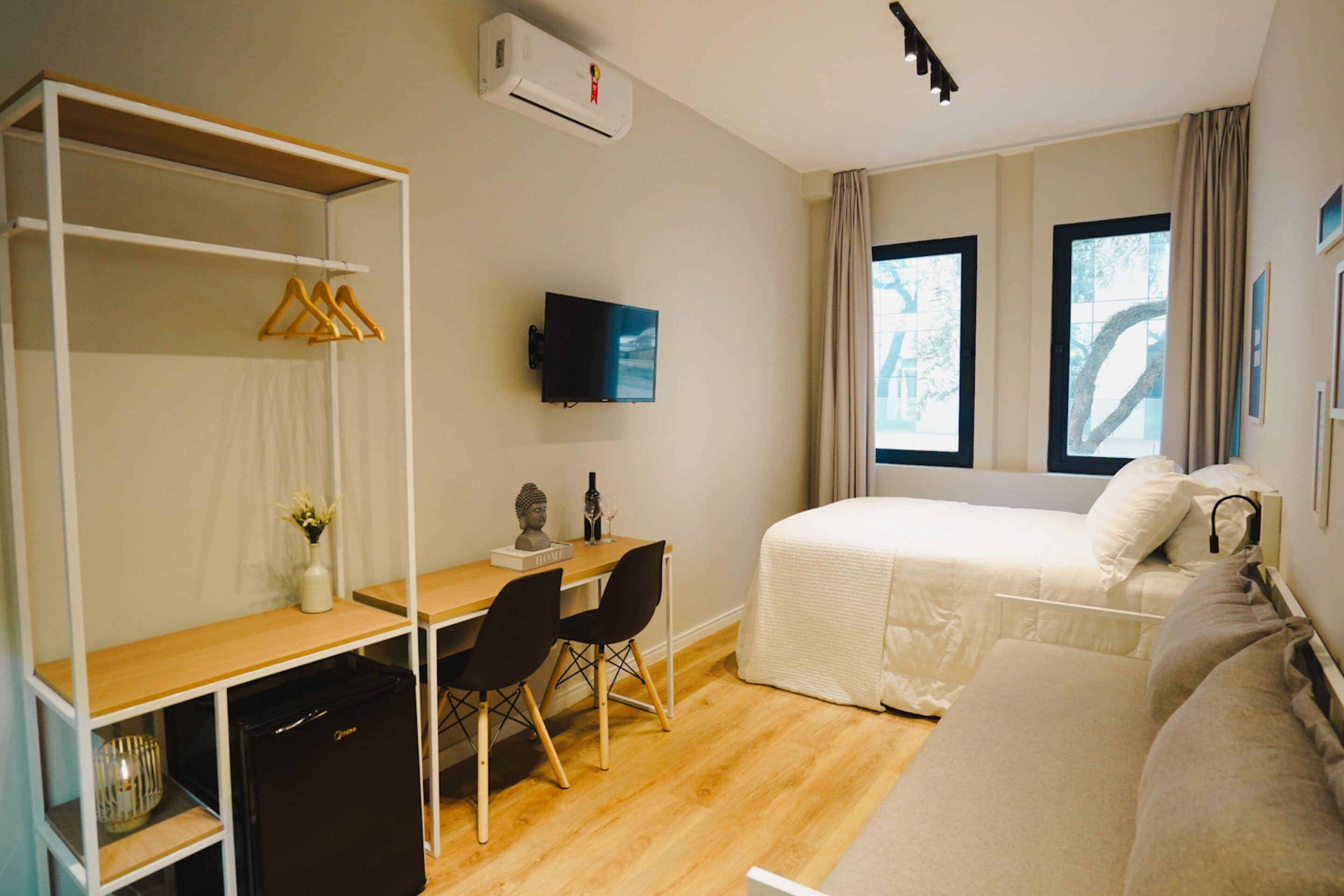 Ein kleines Hotelzimmer mit einem Bett, einem Schreibtisch mit Stühlen, einem Fernseher und einem Kleiderschrank.