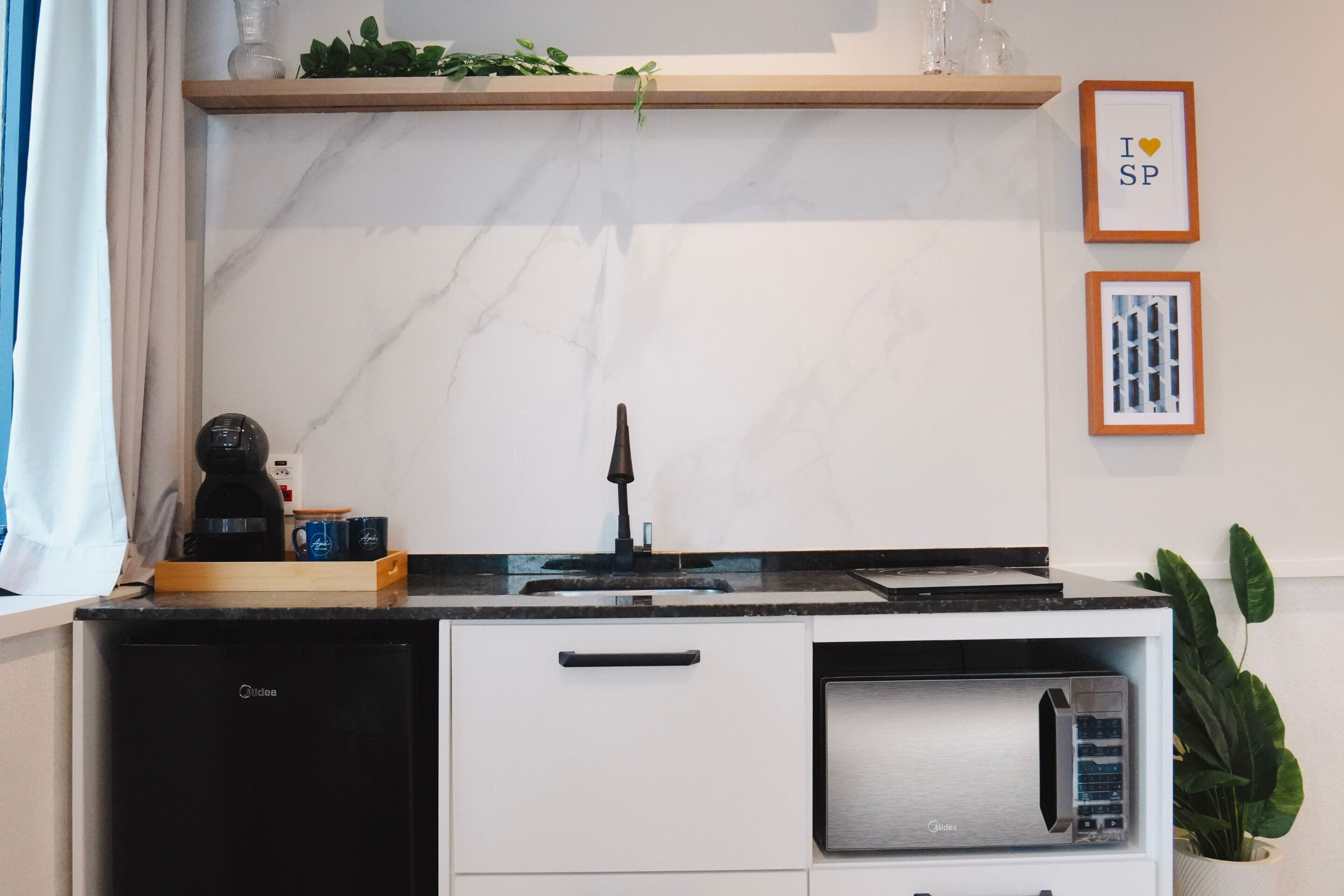 A compact kitchen with a built-in microwave, a coffee machine, and a small refrigerator.