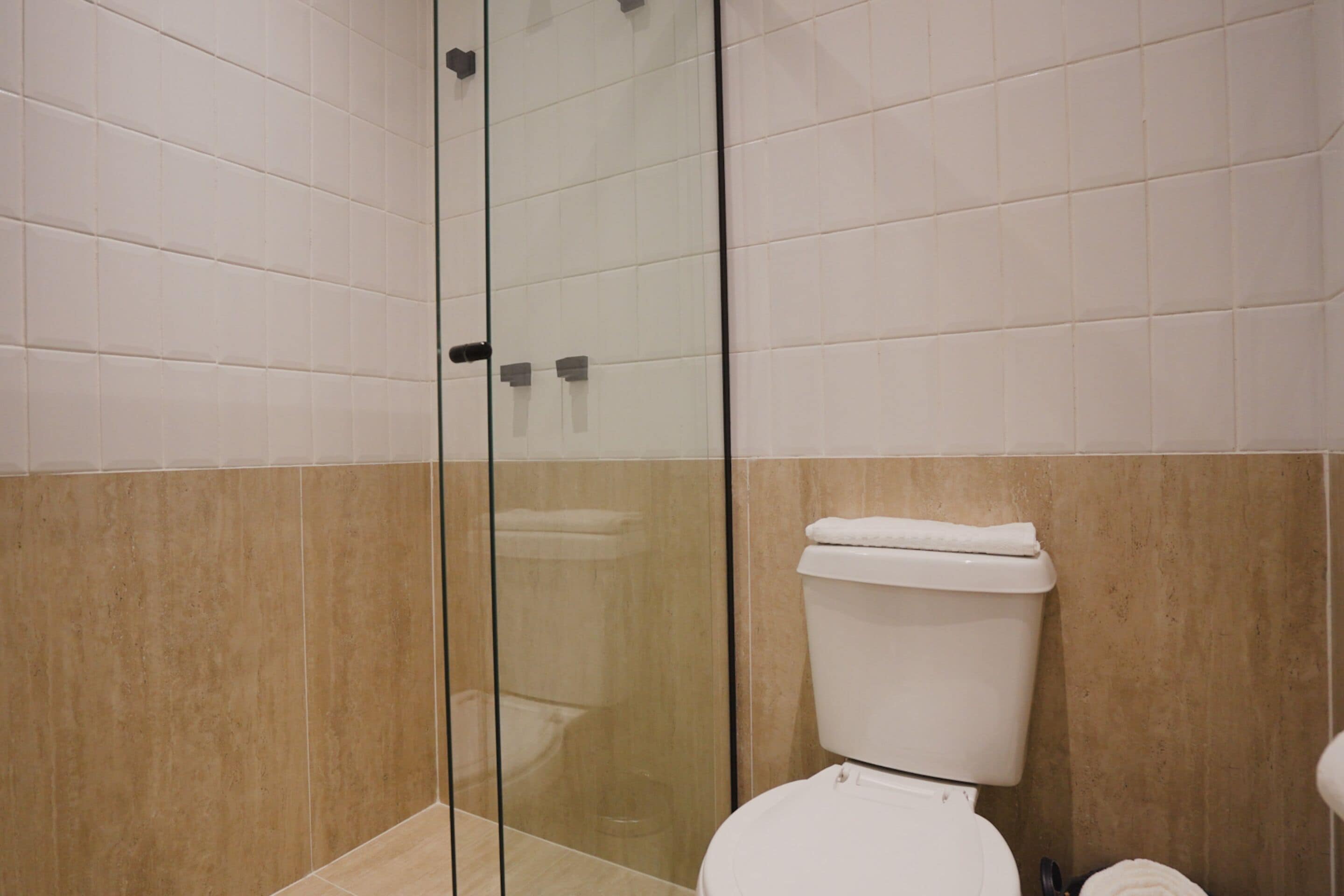 A bathroom with a glass shower enclosure, a white toilet, and beige tiled walls.