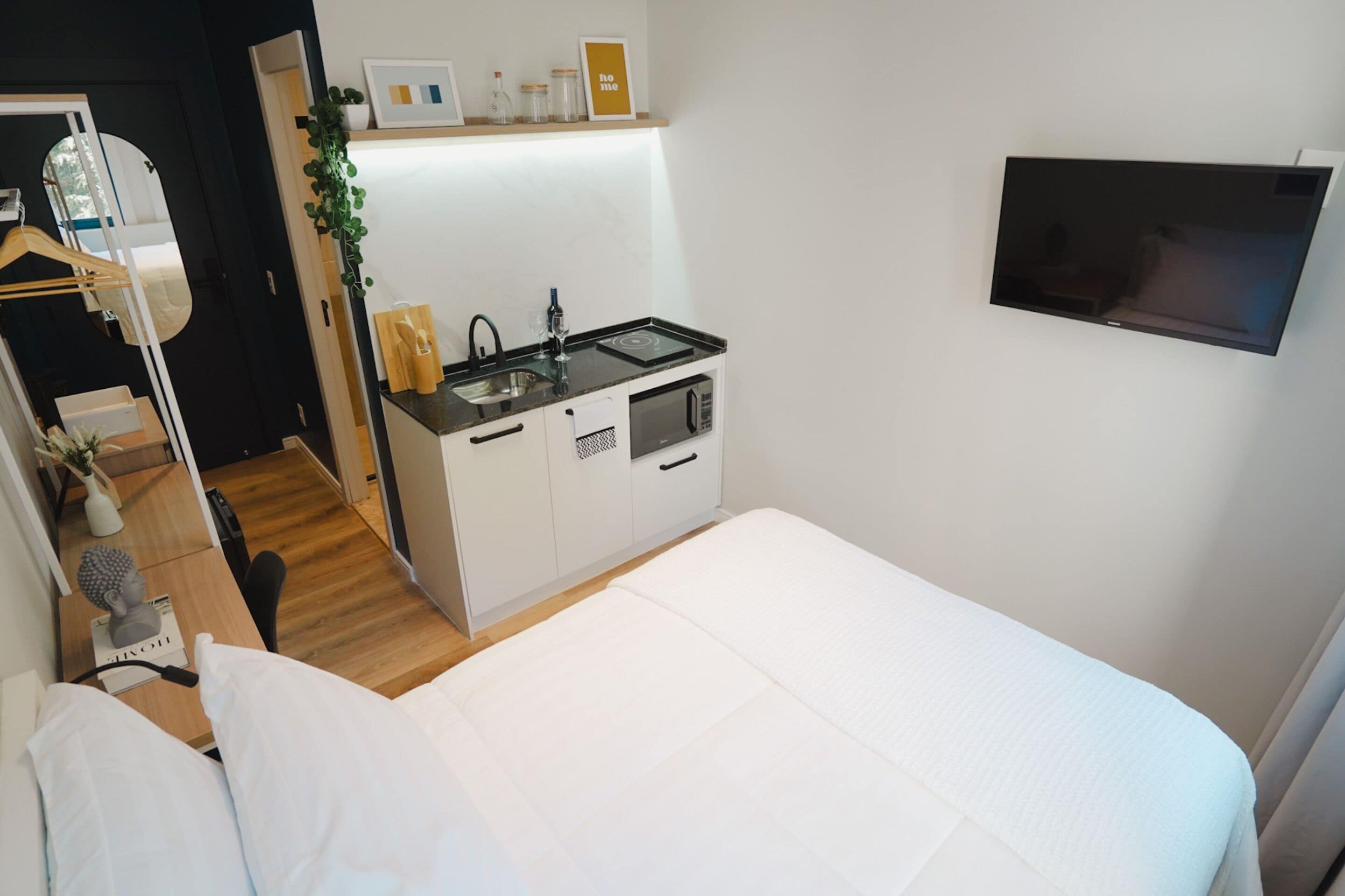 Ein kleines Zimmer mit Bett, einer Küchenzeile, einem Fernseher und einem Bad.