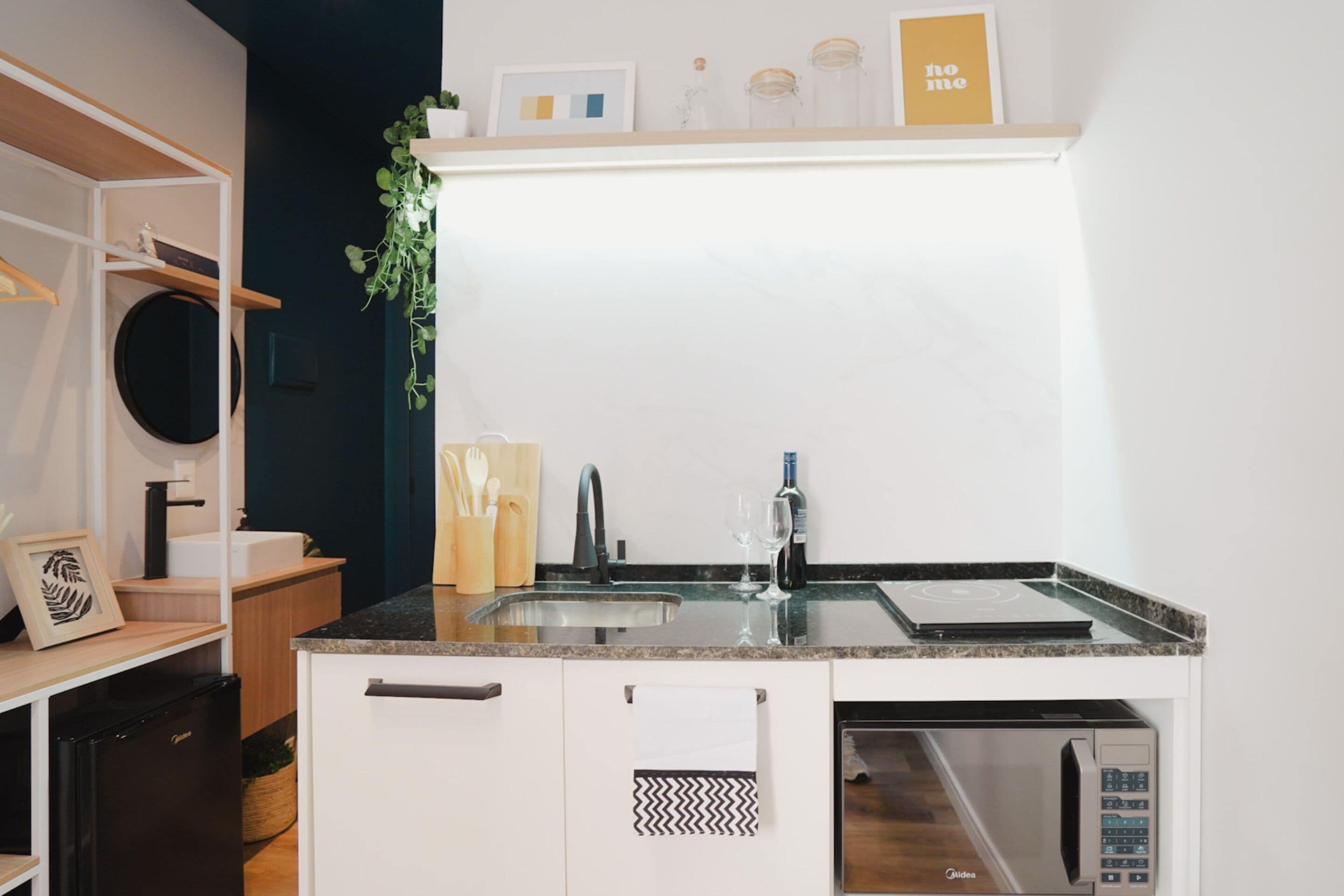 Una cocina moderna con lavavajillas integrado, microondas y fregadero. Encima del fregadero hay un estante de madera con objetos decorativos y un cuadro enmarcado.
