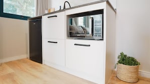 Una cocina compacta con armarios blancos, lavavajillas integrado y una ventana con cortinas.